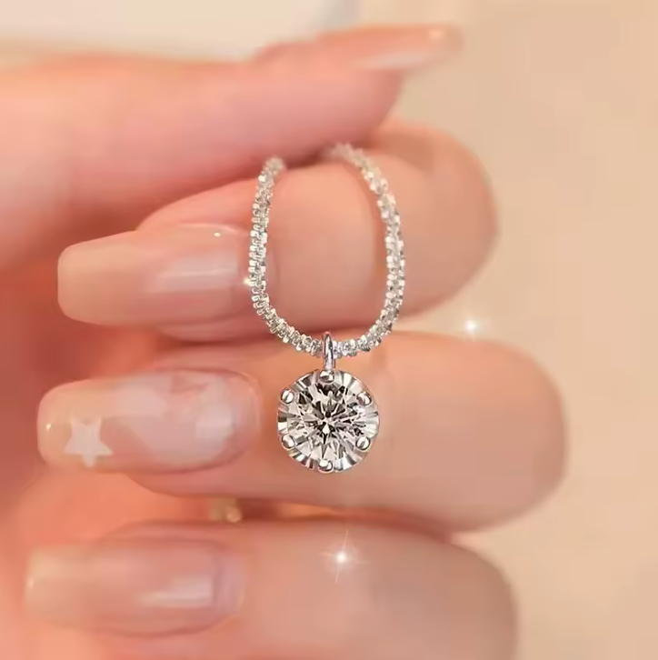 Round solitaire pendant held between fingertips
